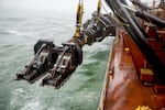 Massive dredge arms are lowered over each side of the ship. They drag along the bottom, sucking up sand to clear the navigation channel.