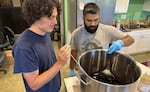 From left, Elderberry Wisdom Farm intern Joaquin Ocana and urban forest coordinator David Mora-Flores check the temperature and consistency of syrup made from pressed blue elderberries.