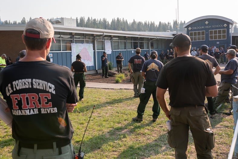 Firefighters stand clustered outside a school building.