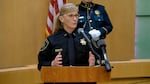 A woman wearing a sheriff's uniform, a long grey/blonde ponytail and glasses speaks in front of a lectern