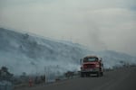 A fire truck driving past smoldering hills.