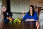 A woman in a blue shirt sits around a table speaking with community members.