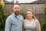 Ben and Sarah Brewington pose for a portrait in their backyard. Ben has blond hair and a beard. Sarah has long blond hair.
