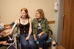 Veronica’s Minneapolis pediatrician takes her blood pressure. Emily sits next to her in the doctor's office. She's wearing a t-shirt that says "Protect Trans Kids" under her khaki jacket.