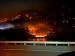 A nighttime view of a wildfire burning in a hill across a river.