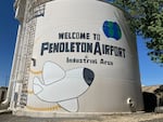 A reservoir painted with a cartoon airplane and globe paired with the words "Welcome to Pendleton Airport & Industrial Area"