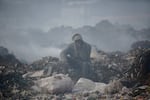 FILE - A man who scavenges recyclable materials for a living rests to smoke a cigarette on a mountain of garage amidst smoke from burning trash at Dandora, the largest garbage dump in the capital Nairobi, Kenya, Tuesday, Sept. 7, 2021. The U.N. health agency said Monday, April 4, 2022, nearly everybody in the world breathes air that doesn’t meet its standards for air quality, calling for more action to reduce fossil-fuel use, which generates pollutants that cause respiratory and blood-flow problems and lead to millions of preventable deaths each year. (AP Photo/Brian Inganga, File)