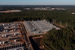 In this 2024 aerial photo, a QTS data center complex on the left side of the frame is under construction in Fayetteville, Georgia. A power substation stands adjacent to it, on the right side of the frame. Green trees surround both sites.