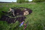 Two Ukrainian boys, wearing battle fatigues and homemade body armor, dig a trench and dugout as they play a war game in the village of Stoyanka, in Kyiv region, on May 11, 2023.