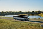 A bus with Greyhound branding in front of a small body of water surrounded by trees