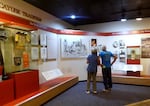 A tourist couple lean toward each other as they look over historic photos, Cayuse artifacts and informational text. Sections of the exhibit are given titles like "The Tragic End" and "The Children."