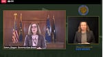 An image of a computer screen shows Oregon Gov. Kate Brown speaking in front of flags on the left of the screen, while a man in a separate window to the right provides sign-language interpretation.