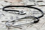 A stethoscope sits on a pile of U.S. bank notes.