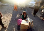 A child crouches on bare ground behind humanitarian aid boxes delivered by UNICEF.