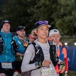 Stephanie Case wears a cap with sunglasses on it and a running vest with water bottles.