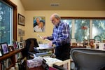A man in a plaid shirt looks at a sheet of paper in his home office.