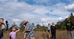 A small crowd of citizen scientists and curious onlookers watches as a monarch butterfly fitted with an electronic tag takes flight. 