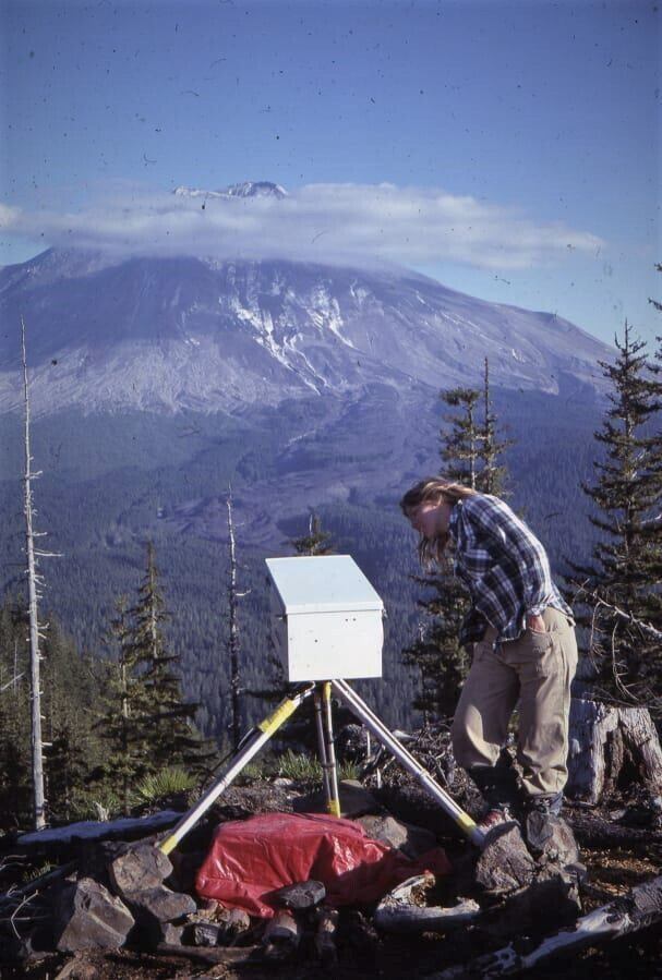 USGS glacier researcher Mindy Brugman peeks at a special timelapse camera set up at the observation post known as Coldwater 2 on May 17, 1980. The resulting images often showed clouds as they swirled around the snow-capped summit of Mount St. Helens, and ever so often, one of the USGS geologists in a frame as they reloaded the camera, including David Johnston who died the next morning in the major eruption of May 18th.