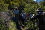 Members of the humanitarian group Borderlands Relief Collective leave non-perishable food and hydration in areas commonly used by migrants walking through rugged terrain on Otay Mountain south of Dulzura, Calif.
