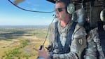 James B. Bartholomees III, wearing sunglasses and a camouflage-print uniform, sits in a Black Hawk helicopter looking out over the terrain of central Luzon island, which stretches out below.