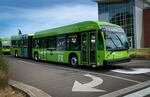 A long green bus with two sections turns waits at a turn signal.