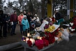 Flowers, candles, and stuffed animals are piled on the seat of a bus stop across the street from where the crews continue to search the apartment building.