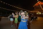 A young couple embraces while their friends take selfies and pictures on the deck underneath the stars.