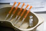 Five syringes are lined up inside a medical pan next to a glass vial of the COVID-19 vaccine.