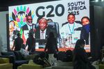 People walk by a large screen TV where South African President Cyril Ramaphosa holds a wooden gavel as he officially closes the G20 leaders' summit, in Johannesburg, South Africa, Sunday, Nov. 23, 2025.