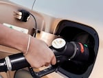 A hand holds a pump that fuels a car.