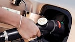 A hand holds a pump that fuels a car.