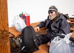 A man sitting at a picnic table with a bicycle and plastic bags.