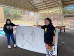 Dezeray, left, and Breonna, right, hold up Breonna's unfinished mural. When complete, Breonna said the mural will show three generations: the elder, the young adult, and the child.