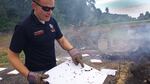 A man stands outside holding a white square and points to one of several charred marks on the square.