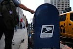 A person drops mail into a blue U.S. Postal Service collection box in New York City in 2020.