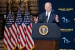 A man stands at a lectern with three U.S. flags behind him.