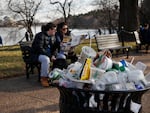 A trash can overflows as people sit outside of the Martin Luther King Jr. Memorial in Washington, D.C.