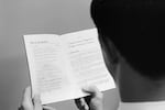 In this black-and-white photo from 1965, a man who is photographed from behind and over his left shoulder is holding a booklet that's opened to a page with the heading "Conscientious Objectors Under Selective Service."