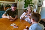 Mary Jo Galusha; her grandson, George; and her son-in-law, Michael Blacketer, sit around a wooden table while they play the card game Uno at her home in Newark, Delaware.