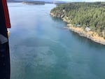 An aerial image looking down at coastal waters that show a sheen of oil.