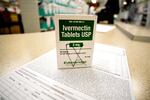 A box of ivermectin is shown in a pharmacy as pharmacists work in the background.