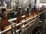 FILE- Bottles freshly filled with beer move on a conveyor belt at Lakefront Brewery in Milwaukee, Jan. 14, 2019. (AP Photo/Carrie Antlfinger, File)