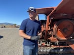 A farmer stands next to a piece of machinery outside during the day.