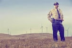 Klickitat County Sheriff Bob Songer stands in a field with wind tribunes behind him.