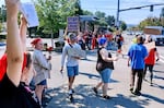 A photo of workers in blue, red, and white clothing standing on a streetcorner, holding signs that say "unfair labor practice" and "union -yes!"