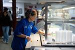 Great Valley School District culinary coordinator Jenifer Halin cleans up the salad bar in the cafeteria at Great Valley High School in Malvern, Pennsylvania. She is wearing a blue chef's coat and has a rainbow bandanna on her head.