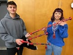Two teenagers both hold up a set of black and red bagpipes in front of a closet.