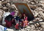 Amid debris, Aicha Ounasser sits with neighbors under a damaged door in Tnirte on Sept. 12.