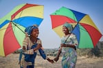 Néema Byanyira (left) chats with Ange Furaha under the shade of their umbrellas. Byanyira says one reason she uses one is to keep her makeup from running.