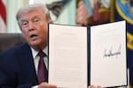 The president sits at a desk and holds up a document facing the camera. 